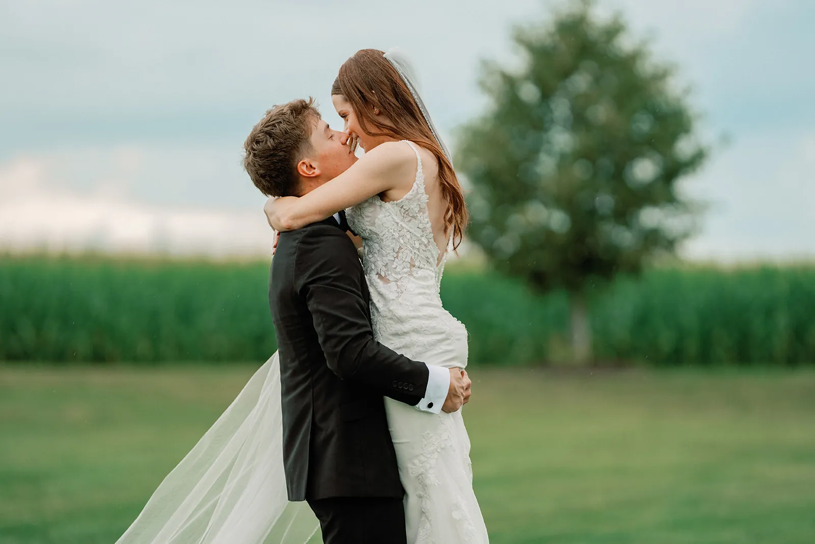 Chris and McKenna kissing beside a lone tree in an open field