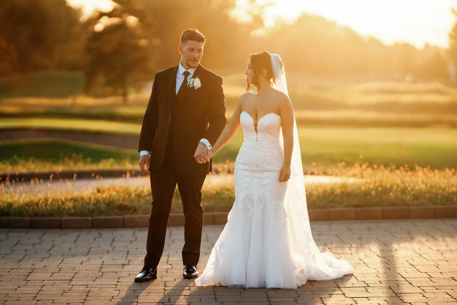A bride and groom holding hands on a stone path at sunset